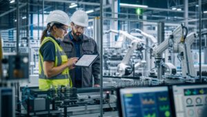Manufacturing engineer and technician reviewing AI-assisted automation beside factory equipment